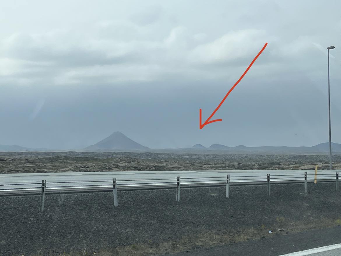 The faint smudge on the horizon is the smoke plume from the erupting volcano.  The mountain behind and to the right is Litli-Hrutur, our vantage point.  The mountain front and left is Kellir.
